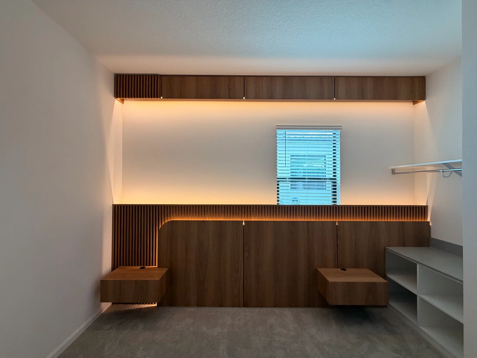 Parede assimétrica de madeira e ripas para quarto com iluminação e criados suspensos.