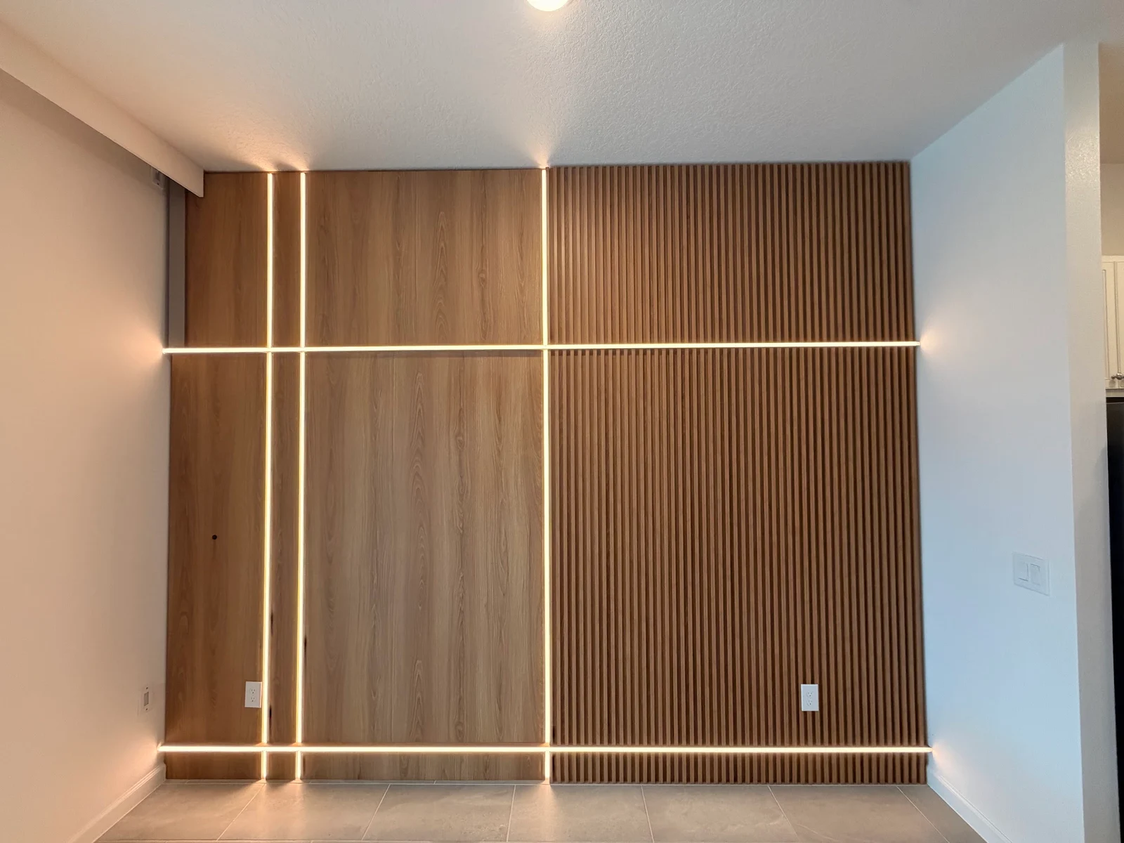 Painel amadeirado do piso ao teto com ripas e iluminação linear integrada.
